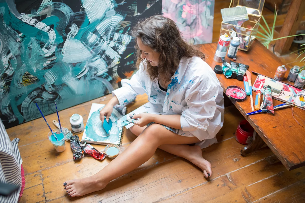 Donna seduta a terra dipinge su tela in modo spontaneo ed espressivo, circondata da colori, incarna la creatività, segnale di individuazione secondo Jung