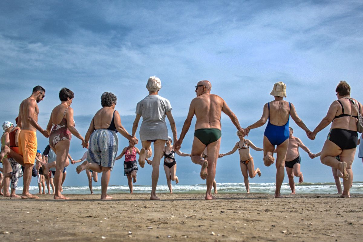 Un allegro gruppo di anziani che si tengono per mano e ballano su una spiaggia sotto un cielo limpido