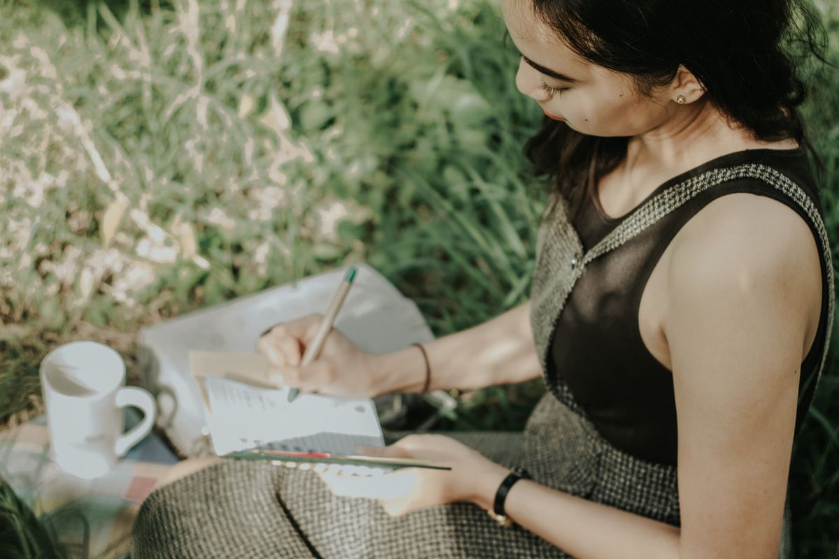 Una donna seduta nell'erba scrive una poesia