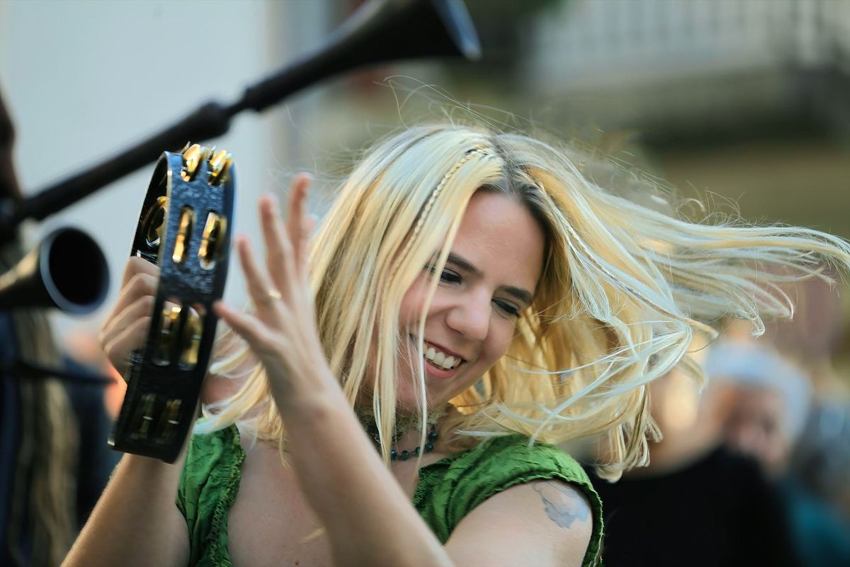 Donna sorridente con capelli biondi che si diverte con la musica, suonando il tamburello